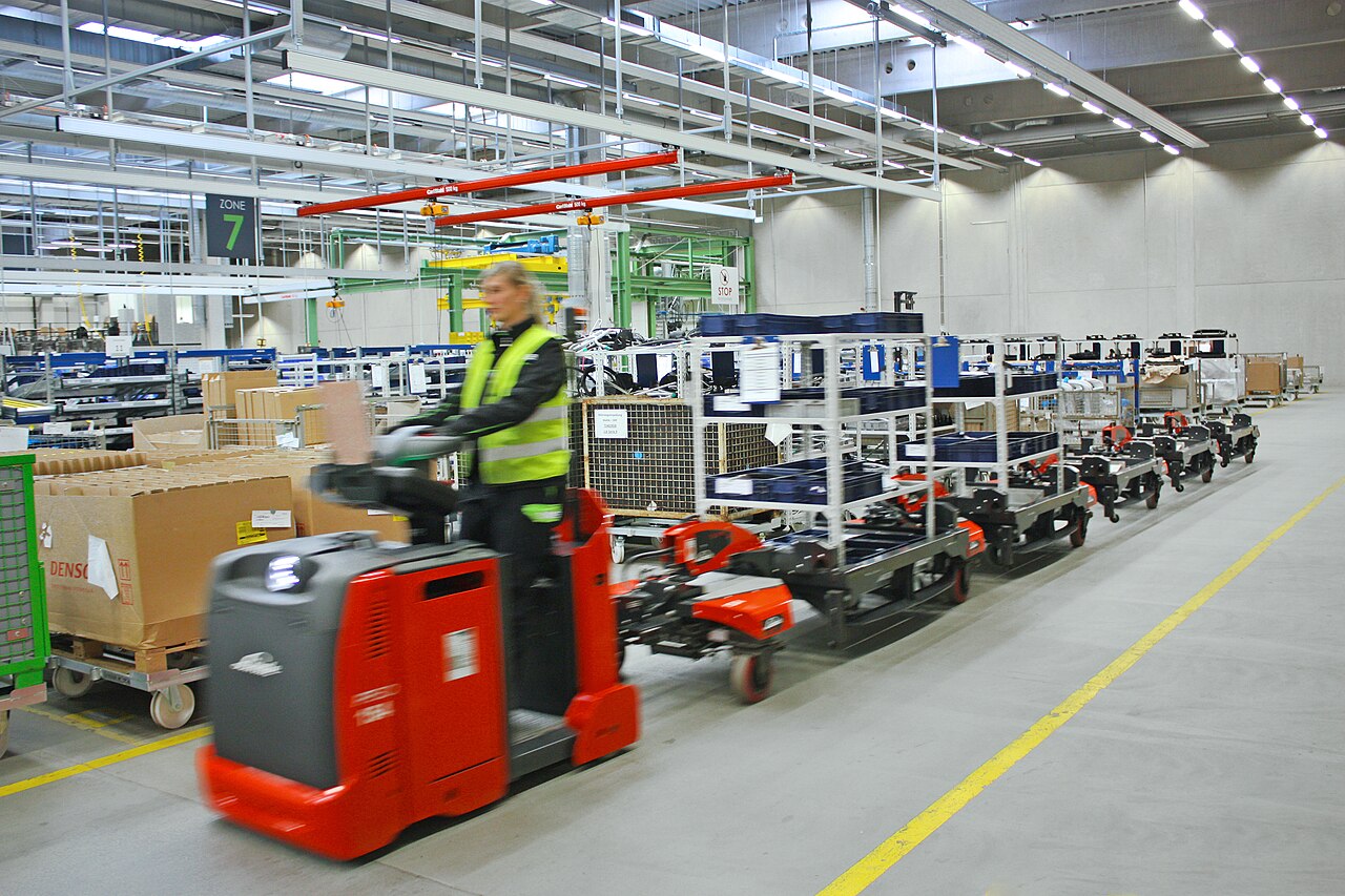 制造设施内工作人员驾驶物料牵引配送车的2018年资料照片