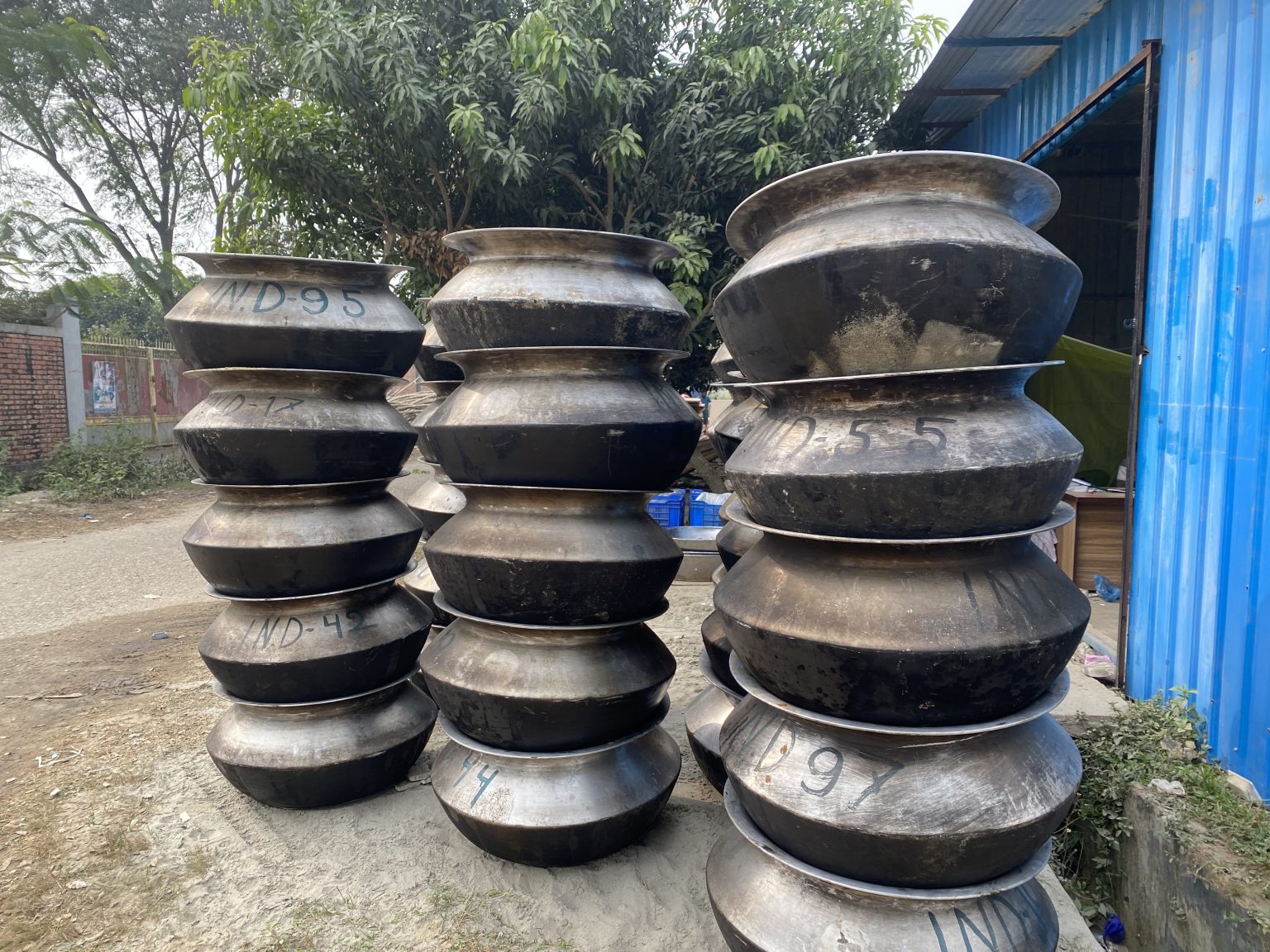 蓝色棚屋旁堆放的大型金属锅,地点及具体金属材质未详
